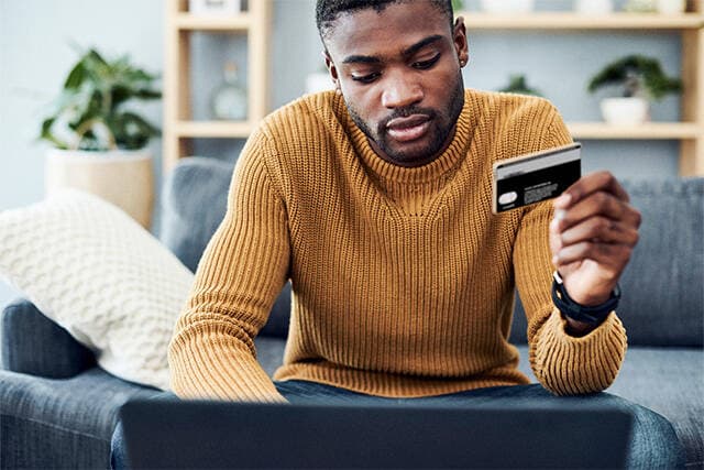 Man sitter vid datorn med sitt Mastercard i handen.