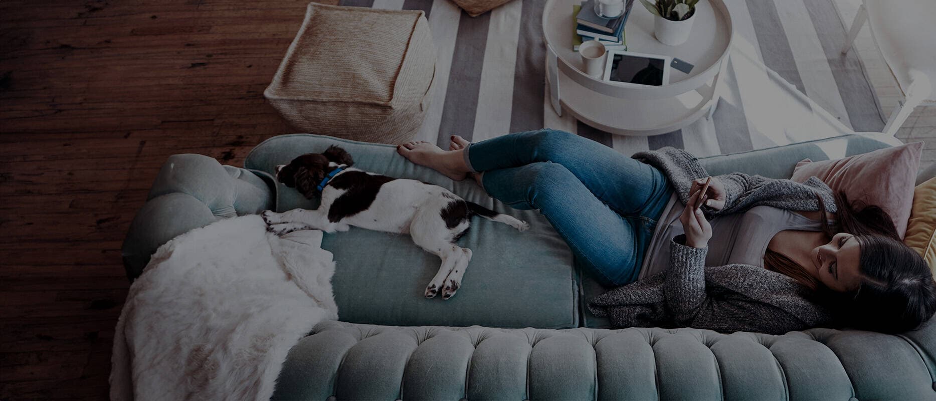 FOtografi på kvinna som ligger i soffan och tittar på mobilen, bredvid henne en hund.